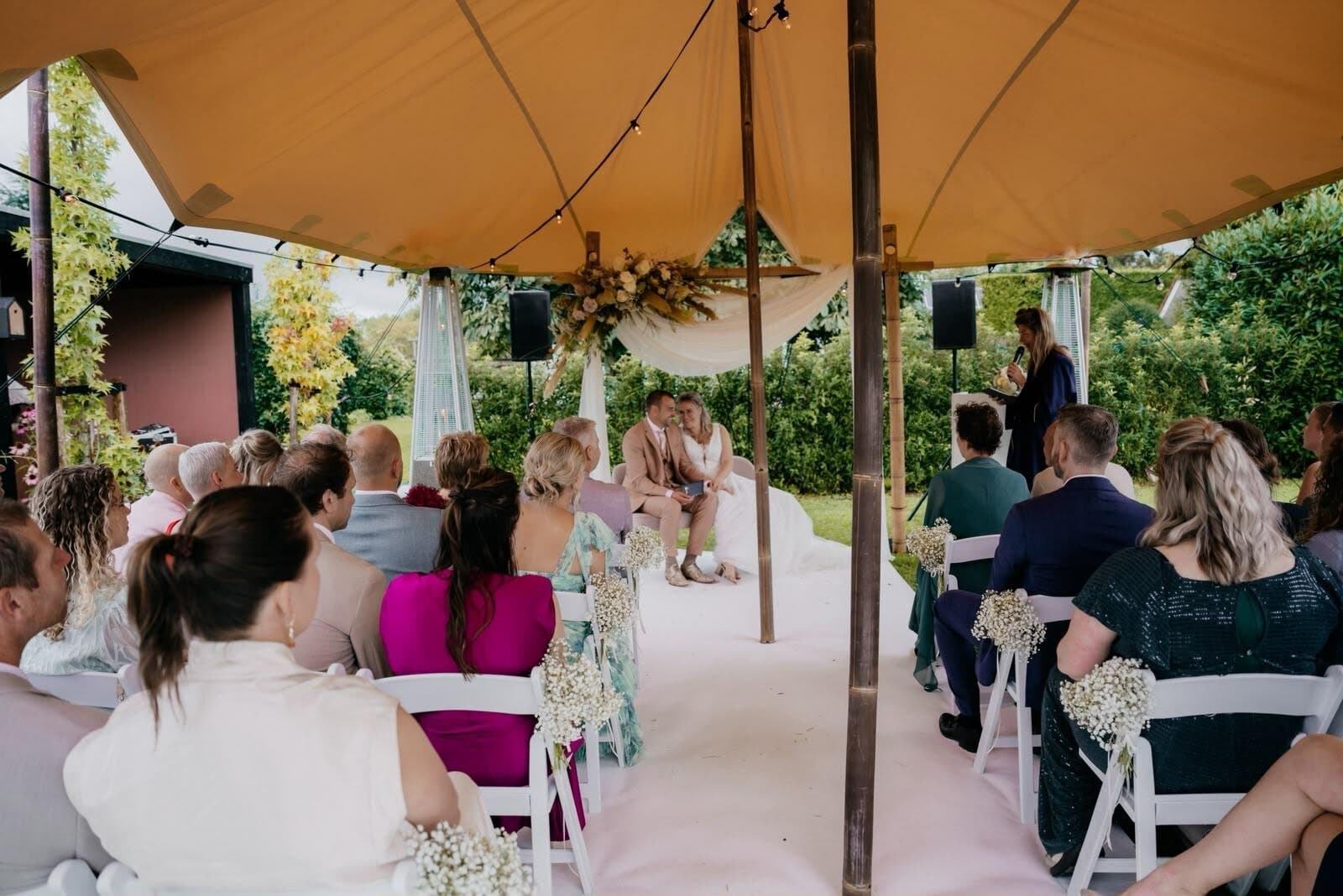 Trouwceremonie onder een beige stretchtent in een tuin