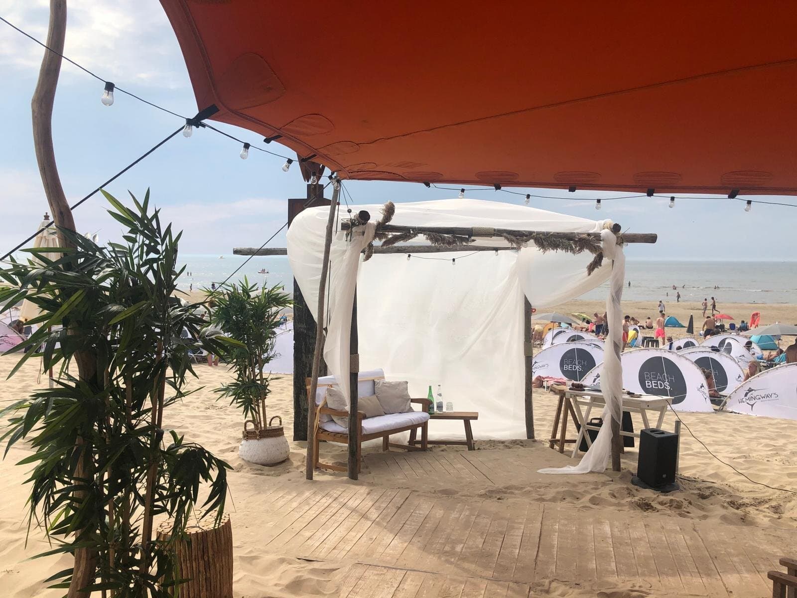 Loungehoek met wit doek onder een oranjerode stretchtent op het strand