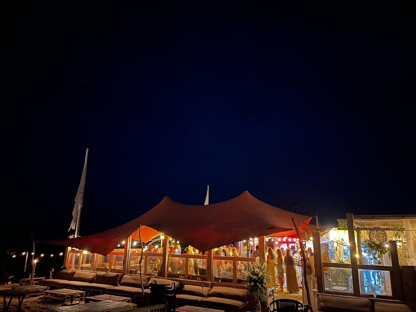 Oranjerode stretchtent met brandende lampjes op het strand bij nacht