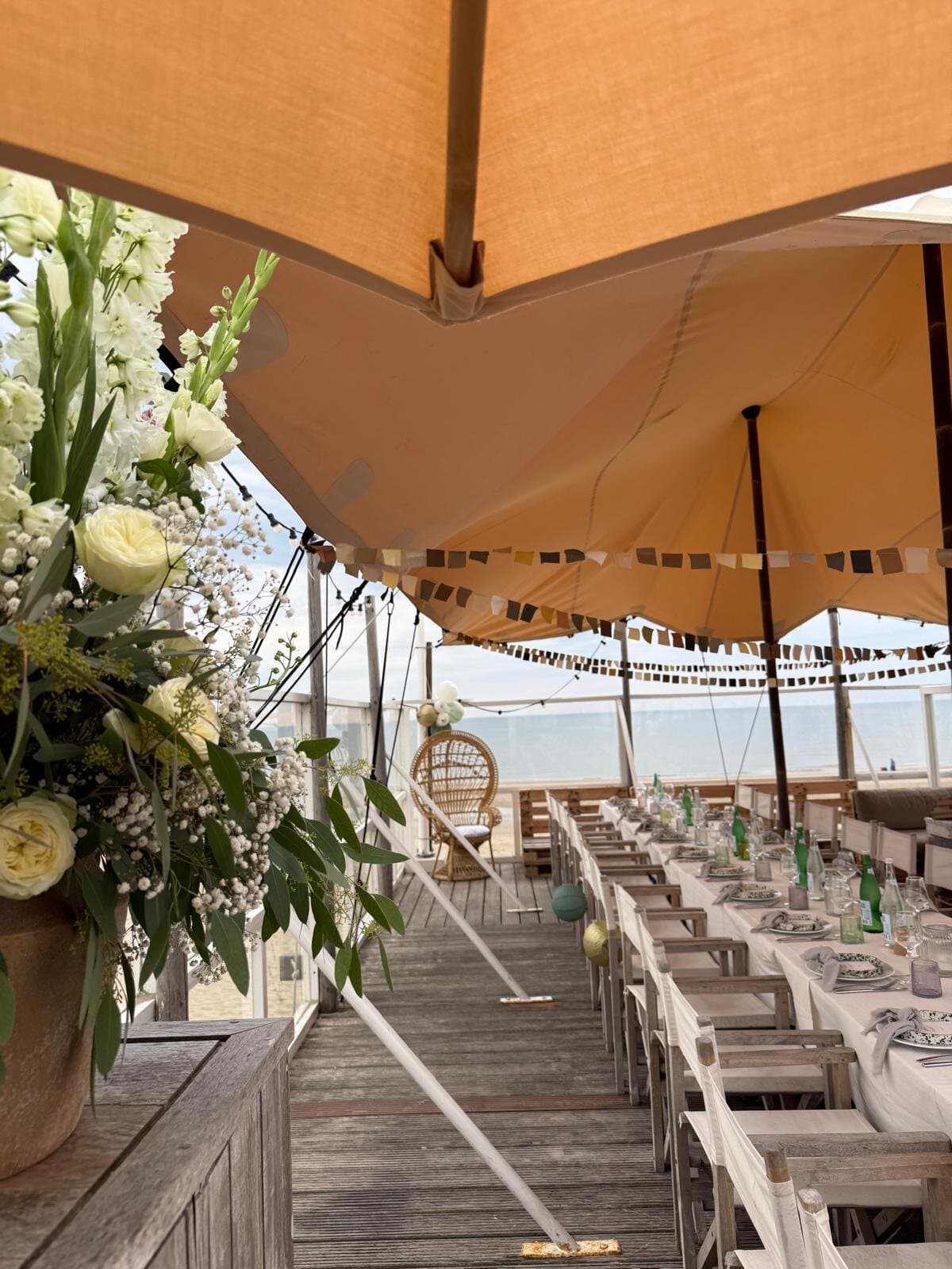Witte bloemen en gedekte tafels onder een beige stretchtent op een strandpaviljoen