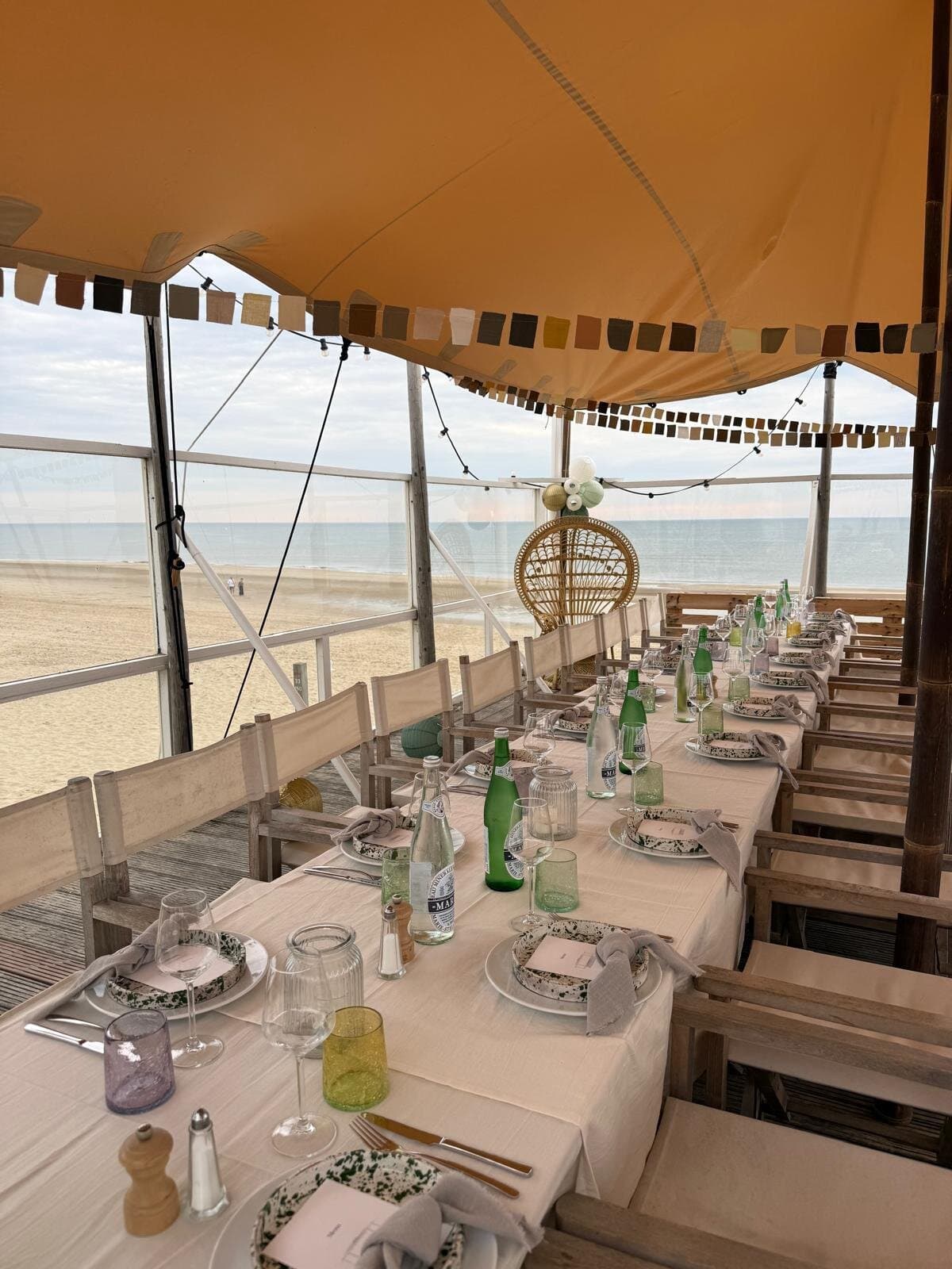 Gedekte tafel onder een beige stretchtent met uitzicht op zee
