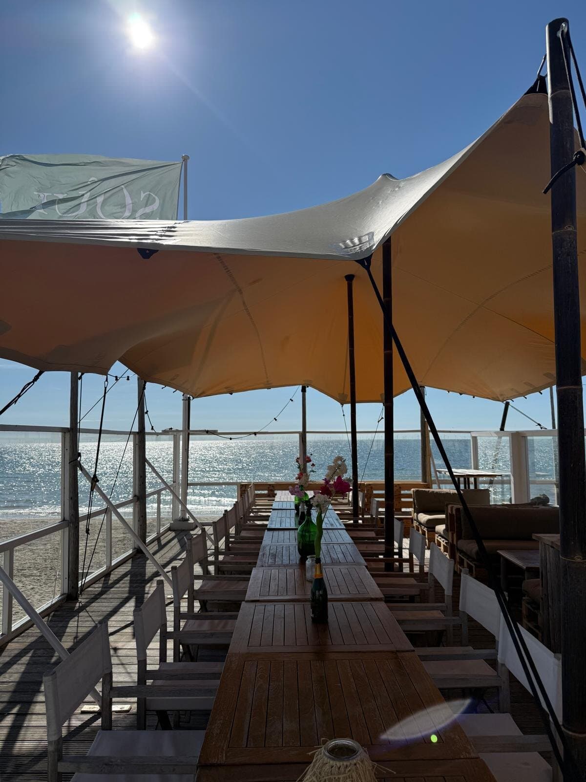 Lange houten tafel onder een beige stretchtent op een strandpaviljoen in de zon